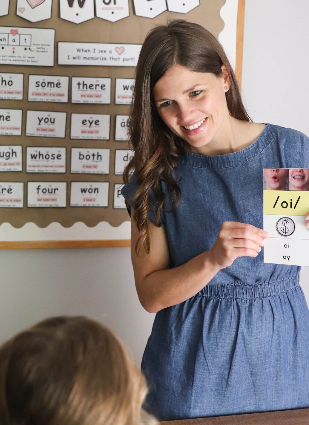 A smiling, brown haired woman holding a diphthong phoneme card.