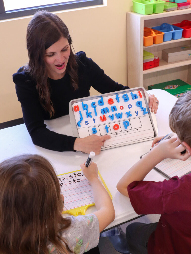 A smiling teacher holding an Elkonin box board with letters.